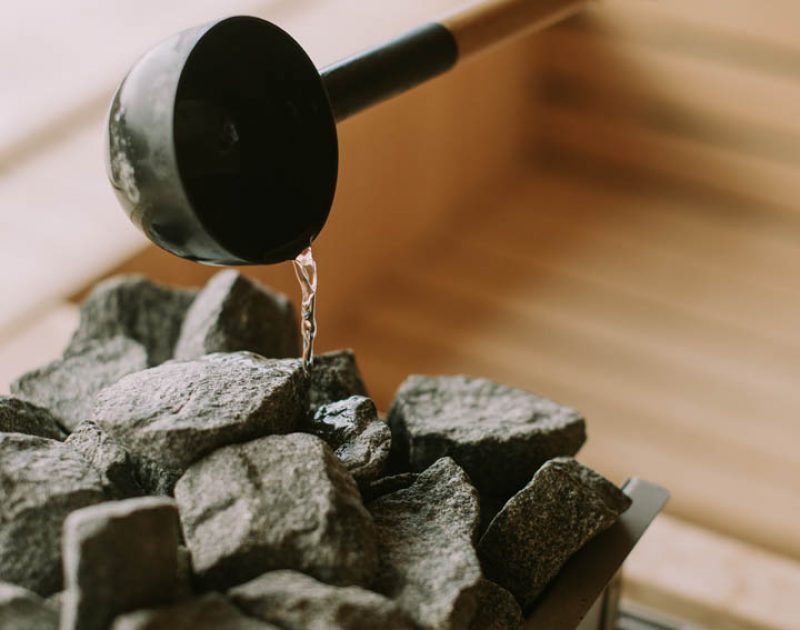 Young woman hand pouring water on hot rocks in the sauna