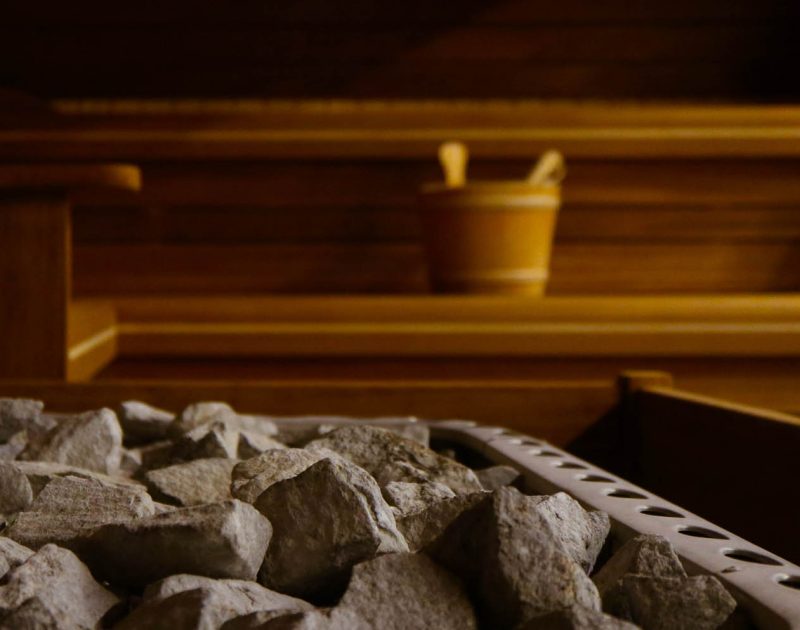 Wooden Bathhouse with a heating pot filled with stones, close up. Wooden sauna interior with equipment, coals, ladle, bucket.