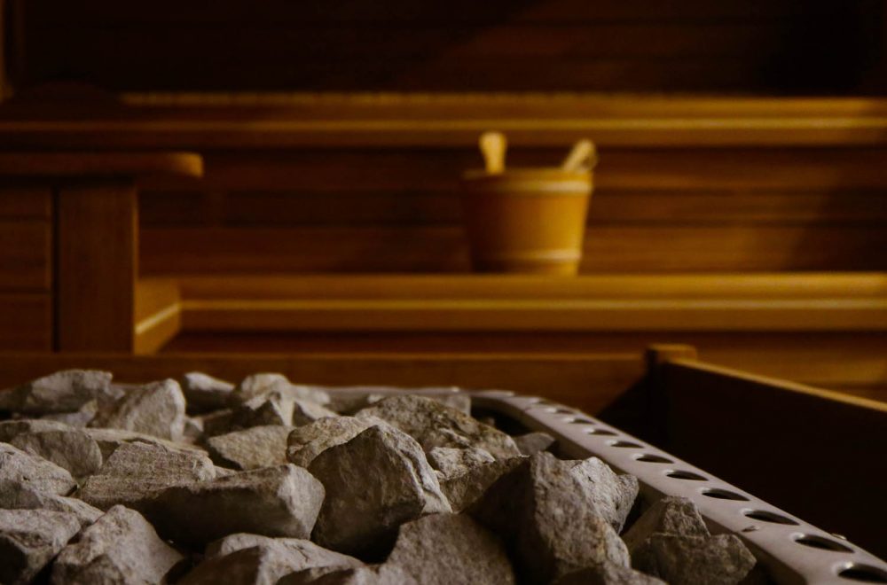 Wooden Bathhouse with a heating pot filled with stones, close up. Wooden sauna interior with equipment, coals, ladle, bucket.